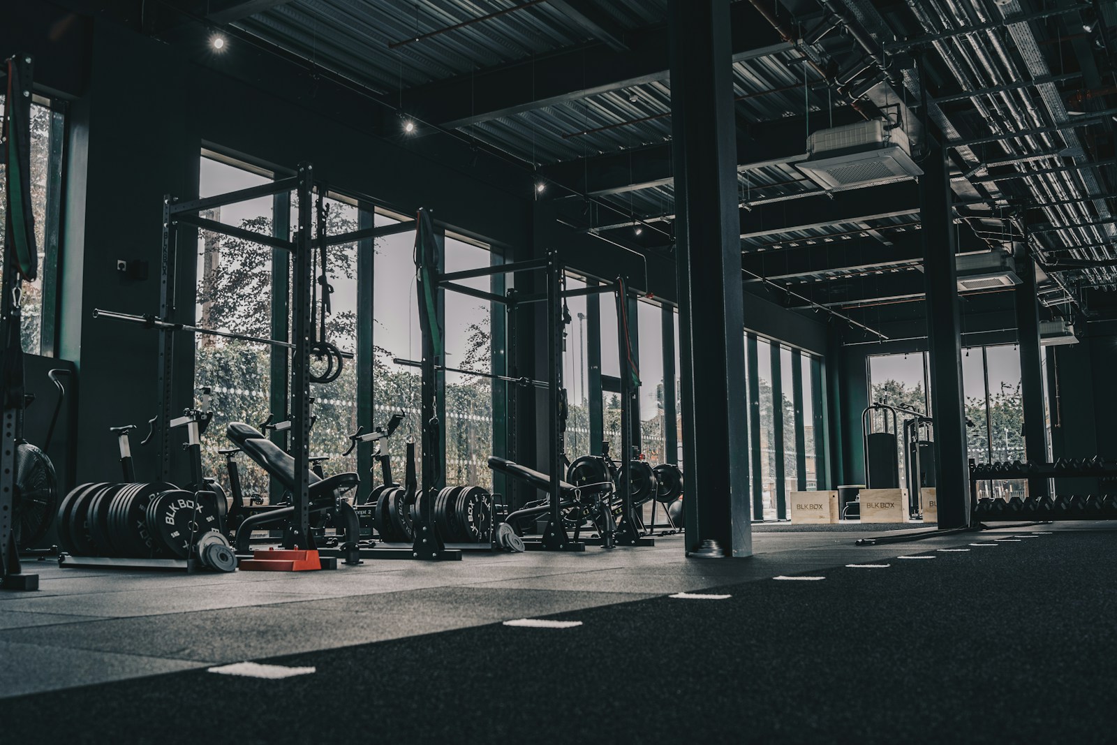 Empty gym floor with squat racks and weight plates in front of tall windows
