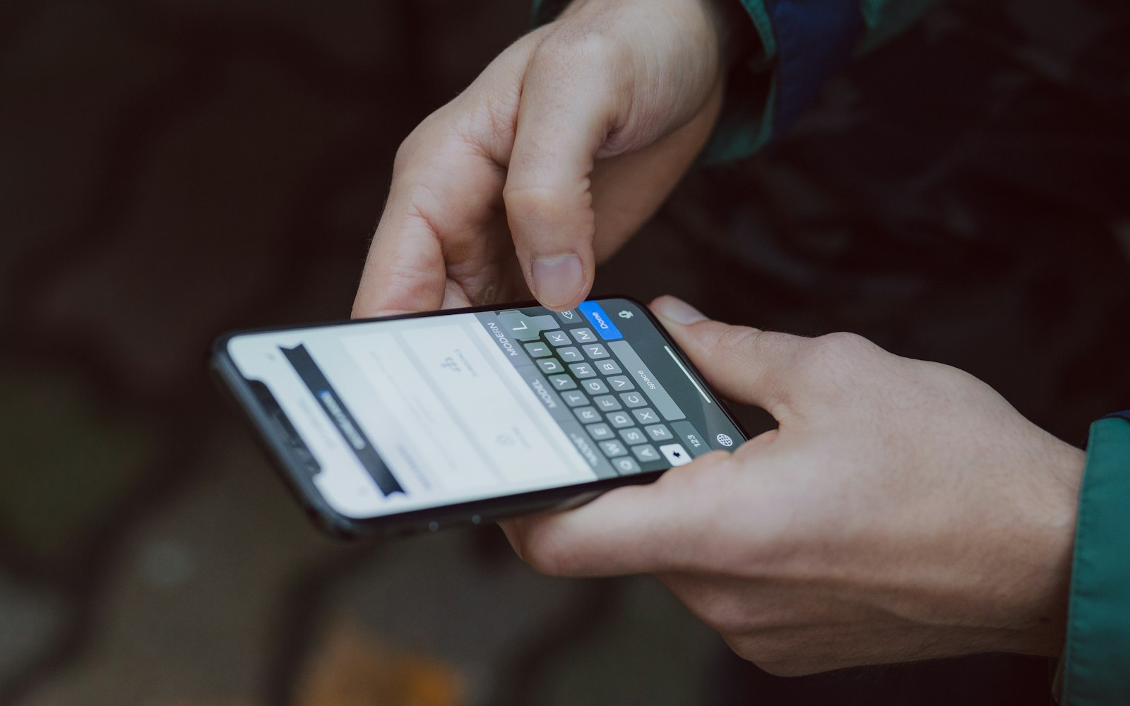 Over-the-shoulder view of two hands holding a smartphone with an on-screen keyboard open, typing into a form