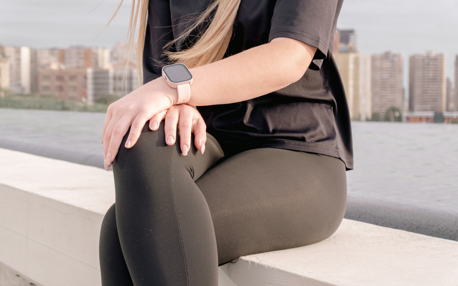 A person in plain black leggings and a plain black t-shirt sitting on a low concrete wall
