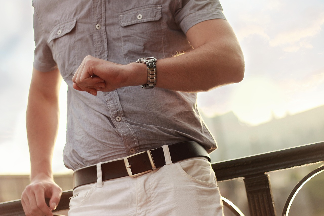 Man in a grey shirt and dark leather belt checking his wristwatch