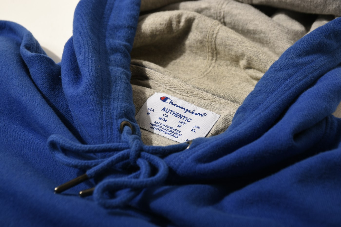 Inside the neck of a blue hoodie showing its sewn-in neck label and the drawcord