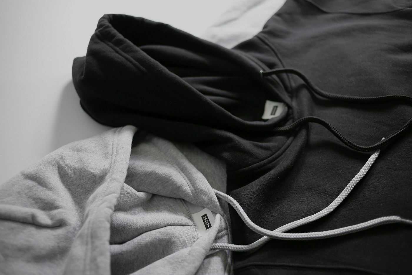 A black hoodie and a grey hoodie lying together with their white drawcords loose