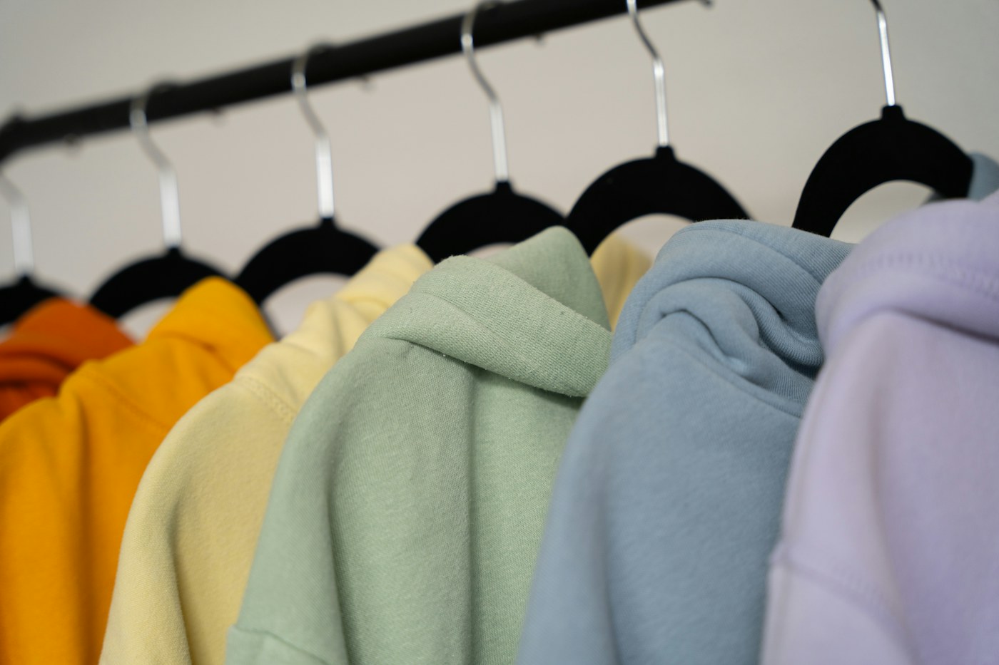 Hoodies in soft yellow, green, blue and lilac hanging side by side on black hangers