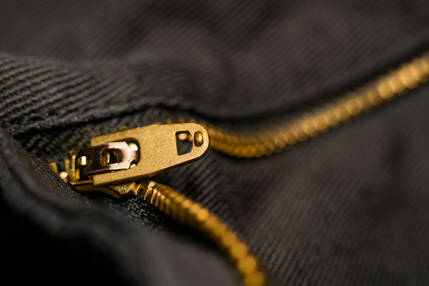 Close-up of a brass metal zipper pull on dark fabric