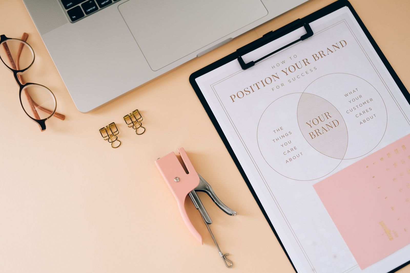 Clipboard with a How to Position Your Brand diagram on a desk next to a laptop and glasses