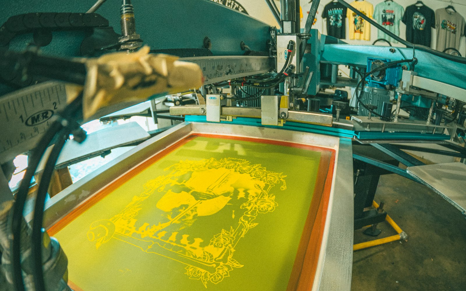 Screen printing press with a yellow design on the screen